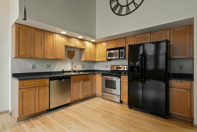 kitchen with sink, stainless steel appliances, a high ceiling, and light wood-type flooring