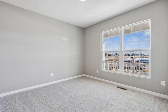 empty room featuring a textured ceiling, carpet flooring, visible vents, and baseboards