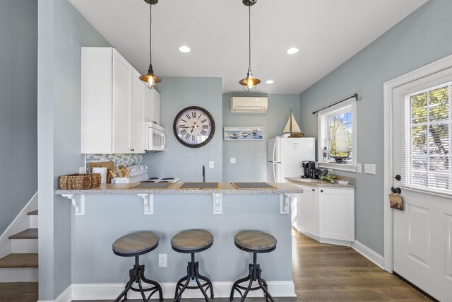 kitchen with kitchen peninsula, white appliances, white cabinetry, and a breakfast bar area