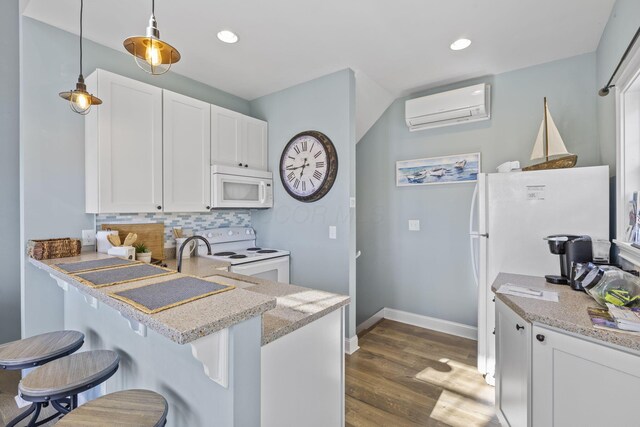 kitchen featuring hanging light fixtures, a wall unit AC, white appliances, a kitchen bar, and white cabinets