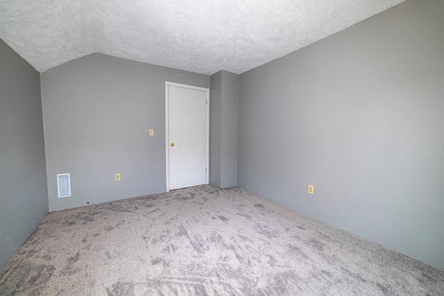 empty room featuring carpet flooring, a textured ceiling, and vaulted ceiling