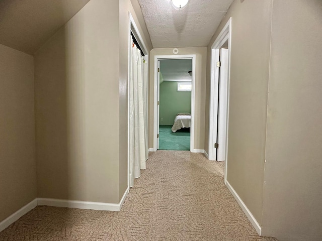 corridor featuring a textured ceiling, light colored carpet, and lofted ceiling