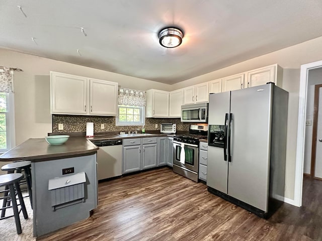 kitchen with kitchen peninsula, appliances with stainless steel finishes, decorative backsplash, dark wood-type flooring, and white cabinetry