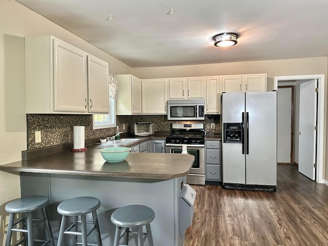 kitchen with dark wood-type flooring, kitchen peninsula, appliances with stainless steel finishes, a kitchen bar, and white cabinetry