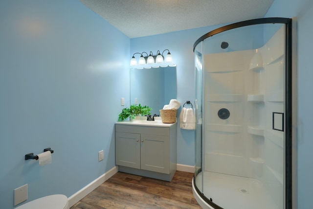 bathroom featuring a textured ceiling, hardwood / wood-style flooring, toilet, a shower with door, and vanity