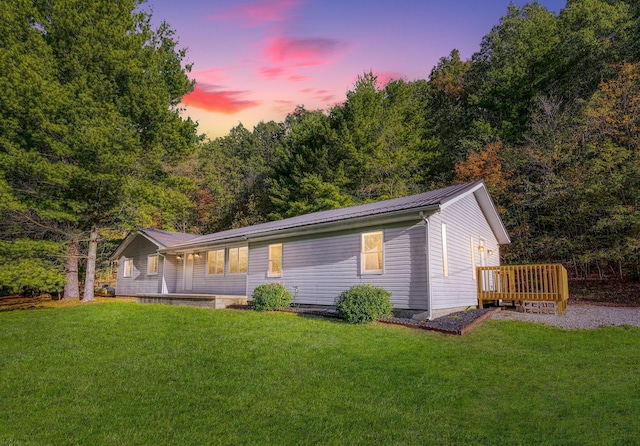 back house at dusk with a wooden deck and a lawn