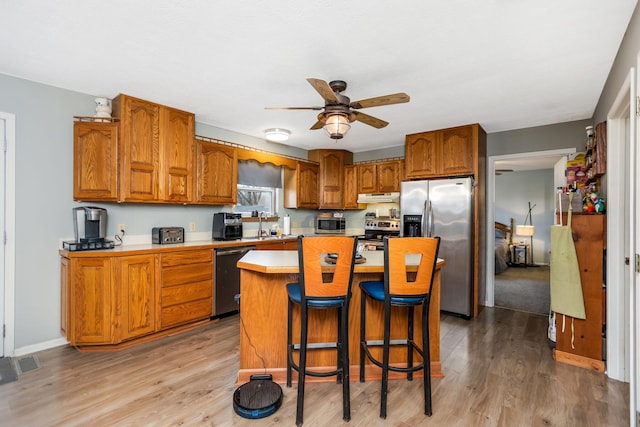 kitchen with a kitchen breakfast bar, ceiling fan, light hardwood / wood-style floors, appliances with stainless steel finishes, and a kitchen island