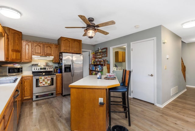 kitchen with a kitchen bar, stainless steel appliances, ceiling fan, wood-type flooring, and a kitchen island