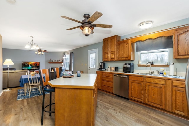 kitchen with sink, light hardwood / wood-style flooring, stainless steel dishwasher, decorative light fixtures, and a kitchen island