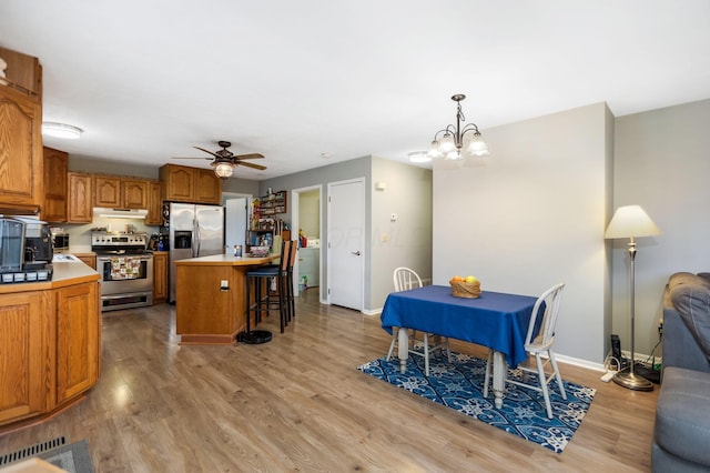 kitchen featuring appliances with stainless steel finishes, pendant lighting, a kitchen island, ceiling fan with notable chandelier, and light wood-type flooring