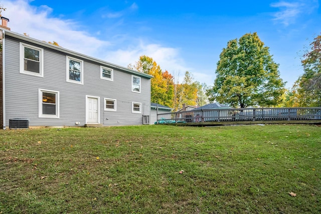 rear view of property with central air condition unit, a wooden deck, and a lawn