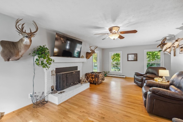 living room featuring baseboard heating, a fireplace, plenty of natural light, and light hardwood / wood-style floors