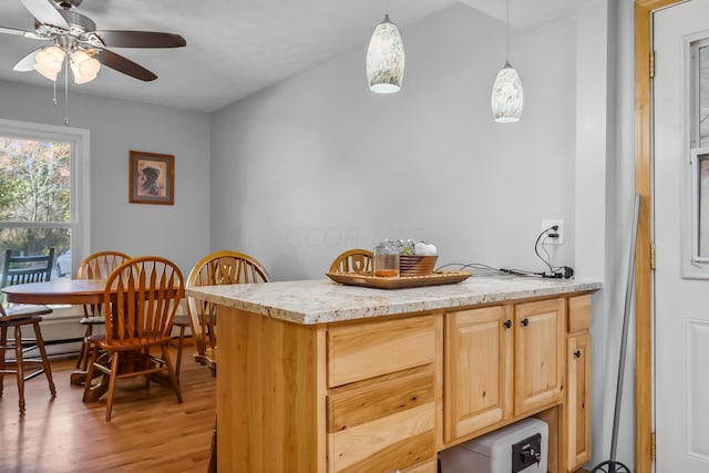 kitchen with light brown cabinets, hanging light fixtures, ceiling fan, light wood-type flooring, and light stone counters