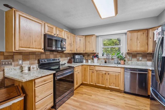 kitchen with appliances with stainless steel finishes, light wood-type flooring, light stone counters, sink, and light brown cabinets