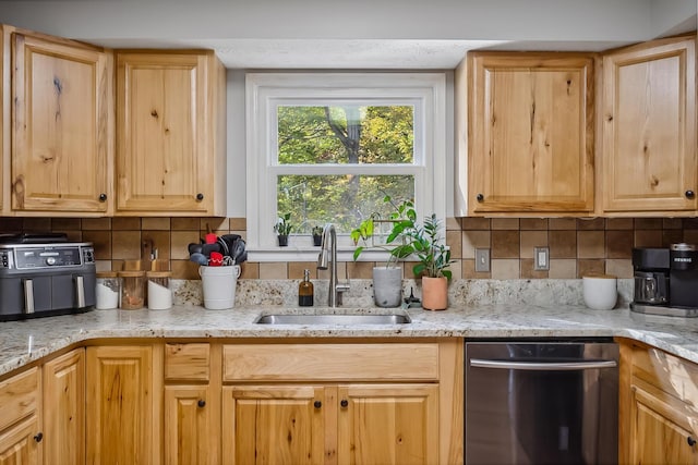 kitchen featuring light stone countertops, backsplash, stainless steel dishwasher, and sink