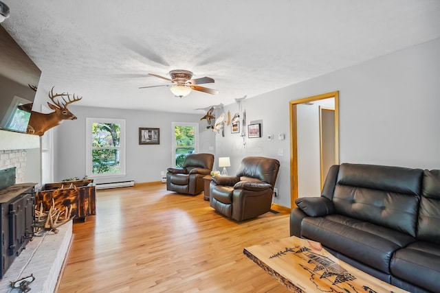 living room featuring a brick fireplace, light hardwood / wood-style flooring, ceiling fan, baseboard heating, and a textured ceiling