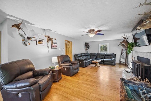 living room featuring ceiling fan, light wood-type flooring, a textured ceiling, and a wood stove