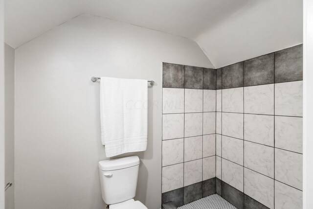 bathroom with toilet, lofted ceiling, and tiled shower