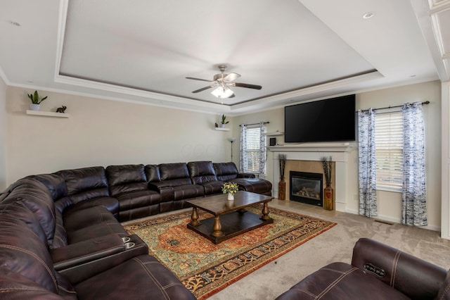 carpeted living room with ceiling fan, a raised ceiling, ornamental molding, and a fireplace