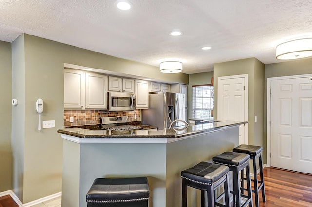 kitchen with backsplash, hardwood / wood-style flooring, a textured ceiling, appliances with stainless steel finishes, and a kitchen bar