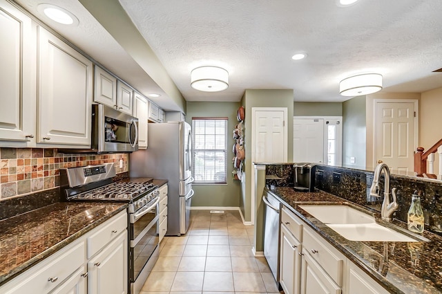 kitchen featuring white cabinetry, sink, stainless steel appliances, dark stone counters, and light tile patterned flooring