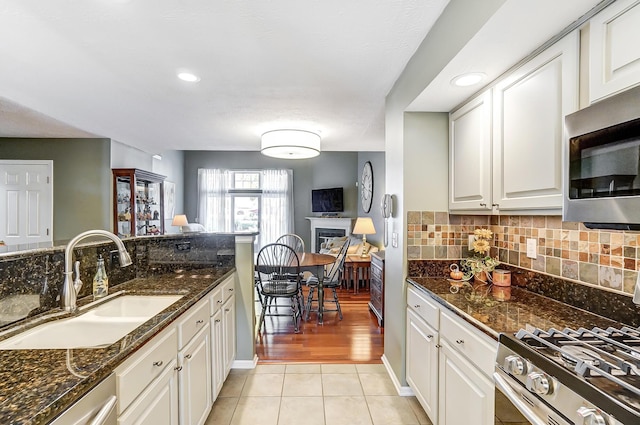 kitchen with sink, light tile patterned flooring, range with gas cooktop, dark stone countertops, and white cabinets