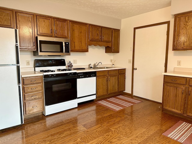 kitchen with a textured ceiling, sink, white appliances, and dark wood-type flooring