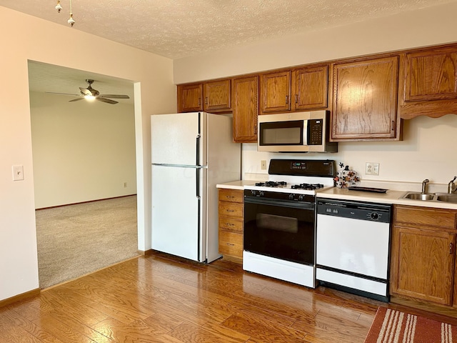 kitchen featuring light wood-type flooring, a textured ceiling, white appliances, ceiling fan, and sink