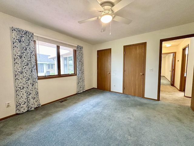 unfurnished bedroom with light carpet, two closets, and ceiling fan