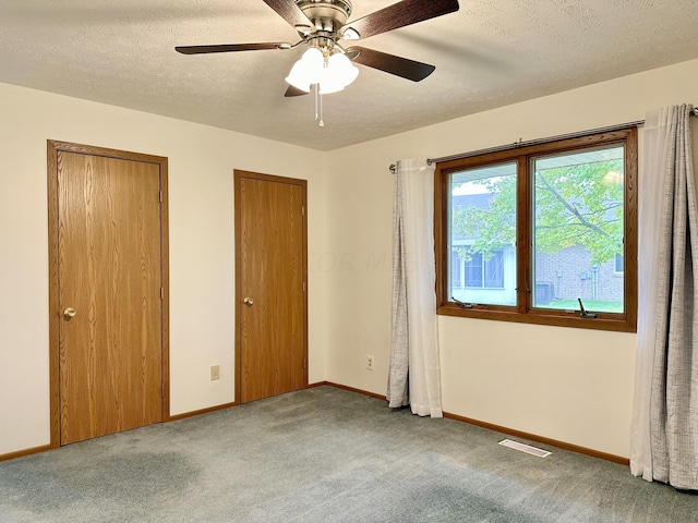 unfurnished bedroom featuring a textured ceiling, ceiling fan, carpet, and two closets