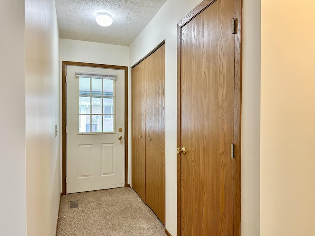 doorway with light colored carpet and a textured ceiling