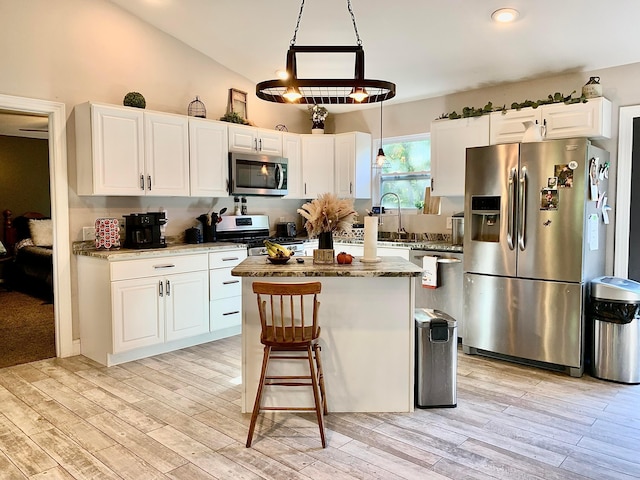 kitchen with appliances with stainless steel finishes, dark stone counters, white cabinetry, a kitchen island, and lofted ceiling