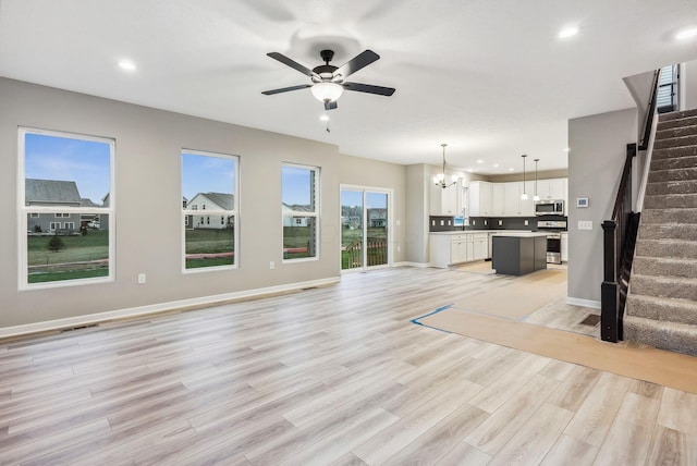 unfurnished living room featuring ceiling fan with notable chandelier and light wood-type flooring