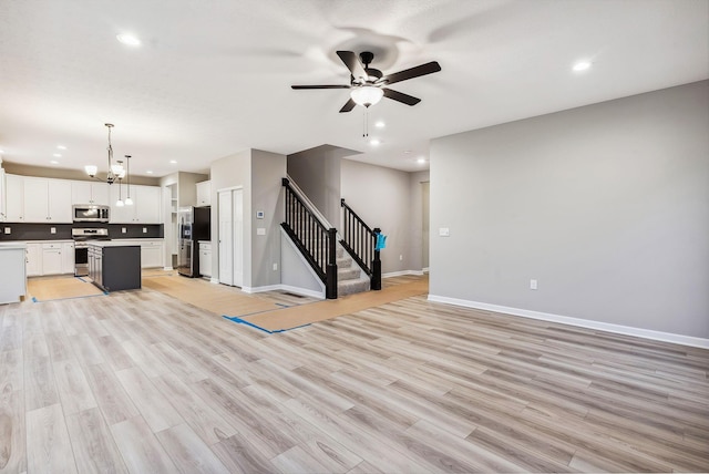 unfurnished living room featuring ceiling fan with notable chandelier and light hardwood / wood-style floors