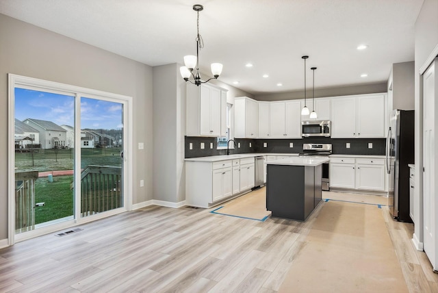 kitchen with light hardwood / wood-style floors, a center island, hanging light fixtures, and appliances with stainless steel finishes