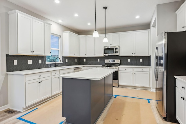 kitchen featuring appliances with stainless steel finishes, tasteful backsplash, decorative light fixtures, a center island, and white cabinetry