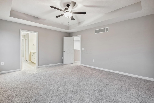 unfurnished bedroom with ceiling fan, a raised ceiling, light colored carpet, and ensuite bathroom