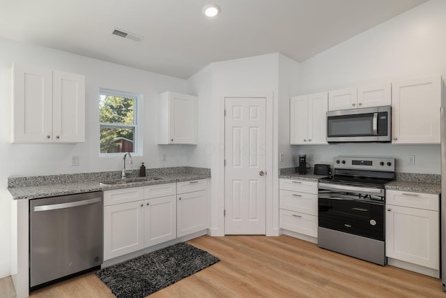 kitchen with lofted ceiling, white cabinets, sink, light wood-type flooring, and stainless steel appliances