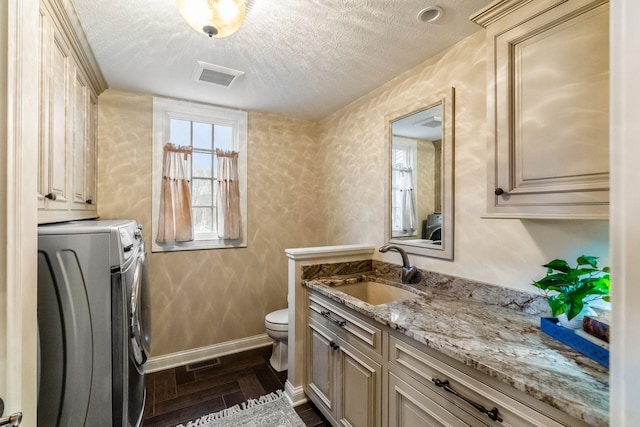 bathroom featuring separate washer and dryer, a textured ceiling, toilet, vanity, and hardwood / wood-style flooring