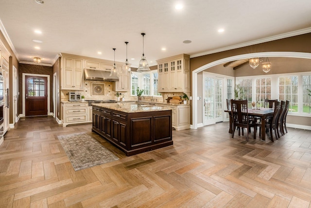 kitchen with light stone countertops, cream cabinets, pendant lighting, dark brown cabinets, and a kitchen island