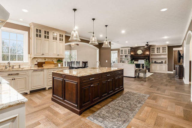 kitchen featuring dark brown cabinets, decorative light fixtures, light stone counters, and a kitchen island