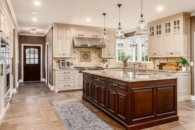 kitchen with dark brown cabinetry, light stone countertops, parquet flooring, crown molding, and a center island with sink