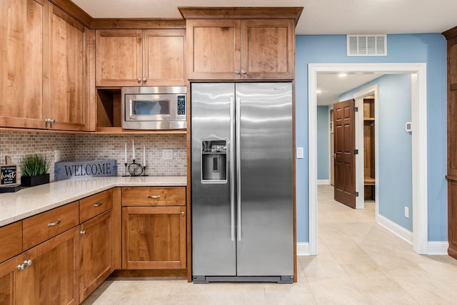 kitchen with light tile patterned flooring, light stone countertops, backsplash, and appliances with stainless steel finishes