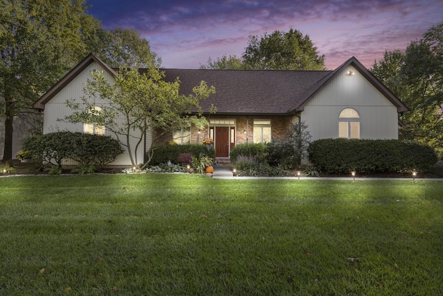 view of front of home with roof with shingles, a lawn, and brick siding