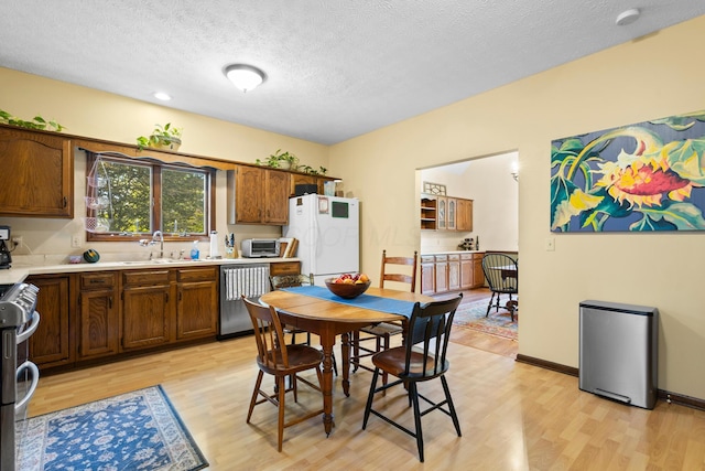 kitchen with a textured ceiling, light wood-type flooring, stainless steel appliances, and sink