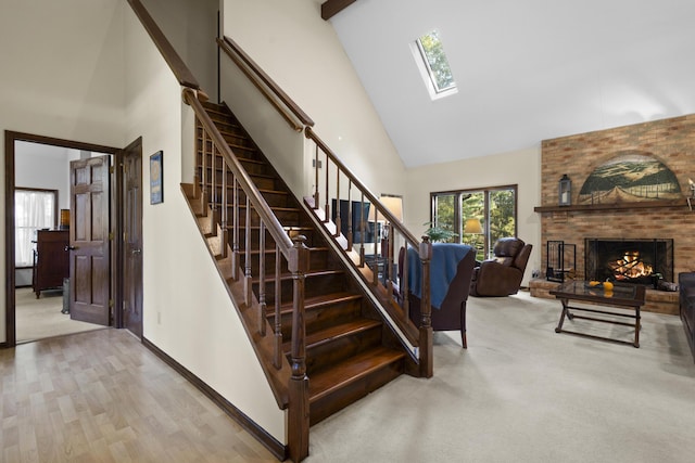 staircase featuring a skylight, high vaulted ceiling, wood-type flooring, and a brick fireplace