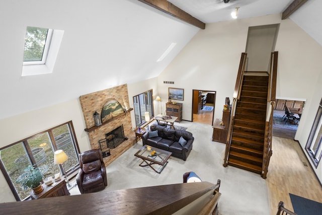 living room featuring light wood-type flooring, a skylight, a brick fireplace, high vaulted ceiling, and beamed ceiling