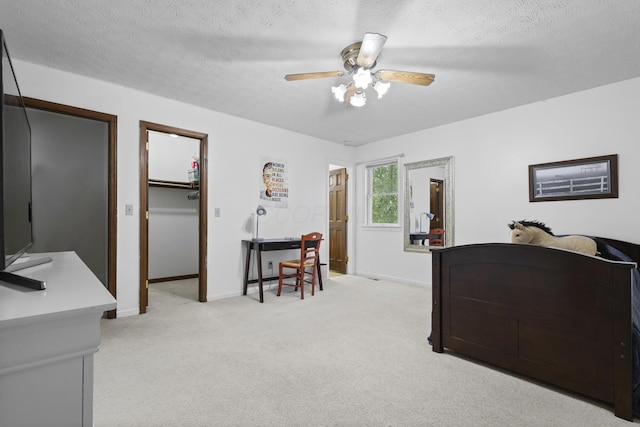 bedroom featuring light carpet, ceiling fan, a spacious closet, a textured ceiling, and a closet