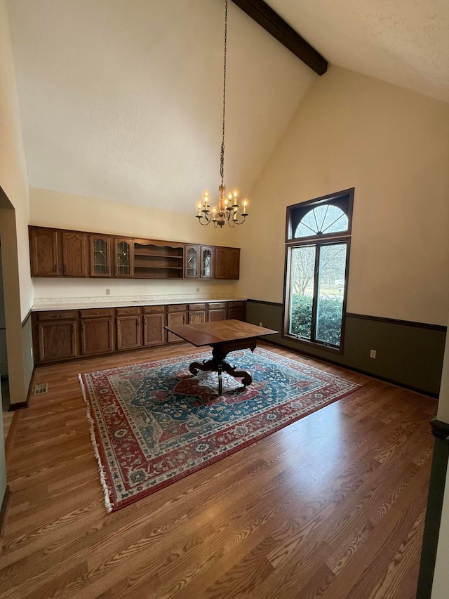 dining area with beam ceiling, a wainscoted wall, a notable chandelier, dark wood-style flooring, and high vaulted ceiling