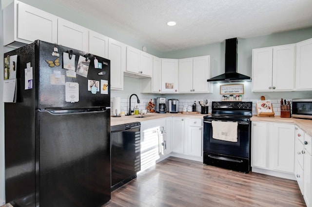 kitchen featuring sink, white cabinetry, wall chimney exhaust hood, and black appliances